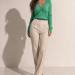 Дамска зелена блуза с V-образно деколте и дълги ръкави, носена от модел в цял ръст, комбинирана с бежов панталон